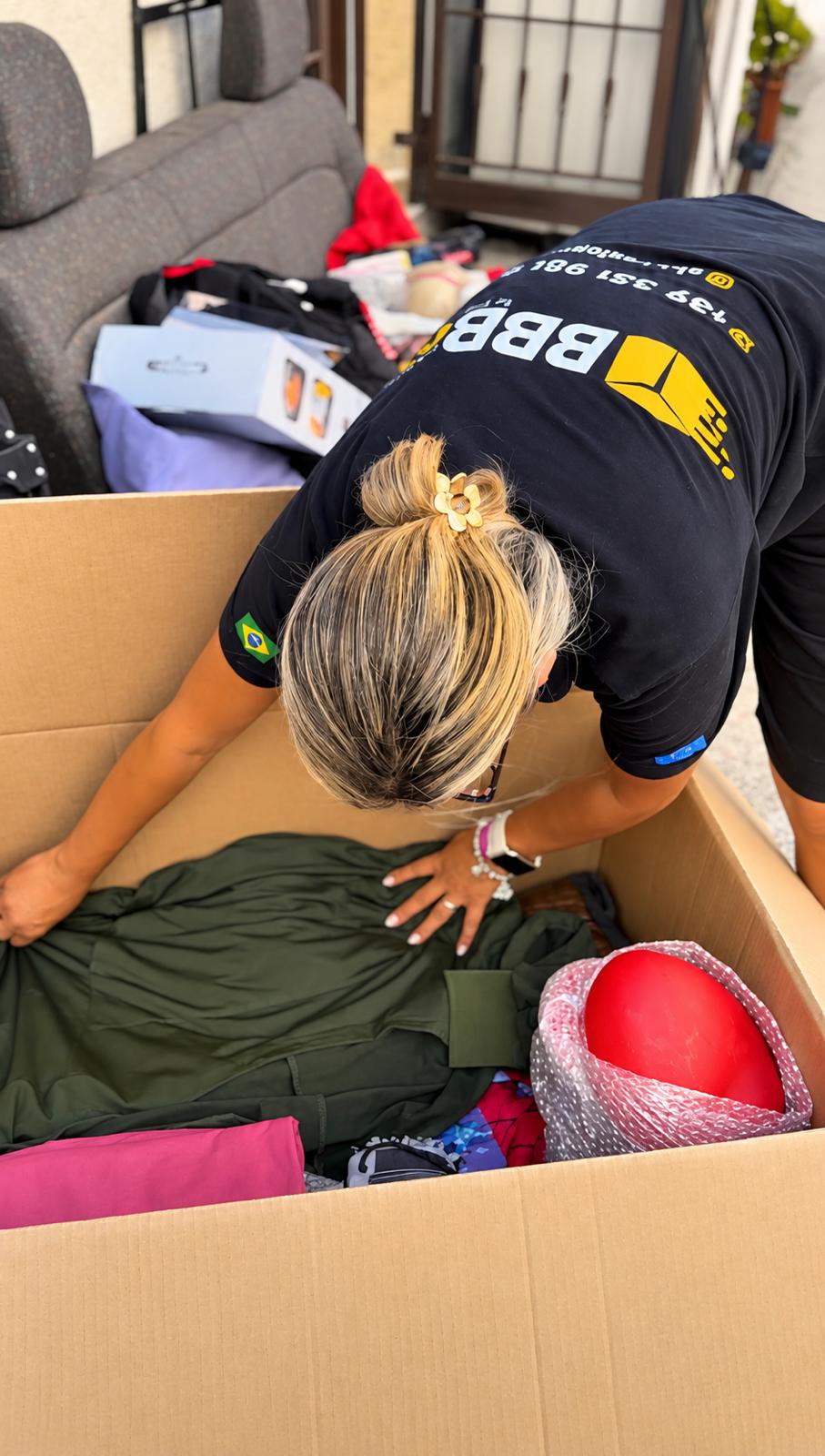 Integrante da equipe com uniforme da BBBox embalando roupas em uma caixa grande