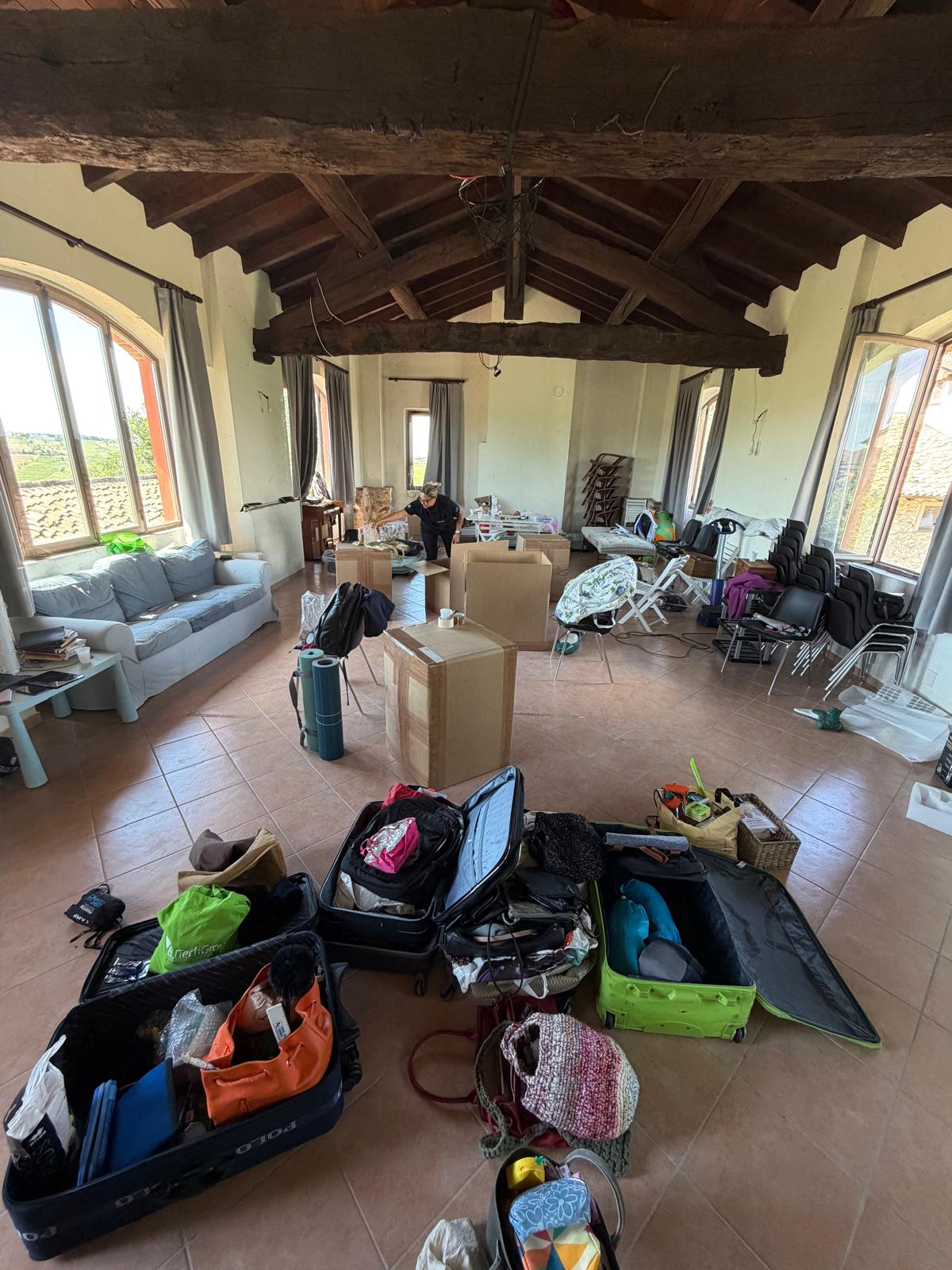 Malas e caixas abertas com roupas e pertences sendo organizados em uma sala com vigas de madeira